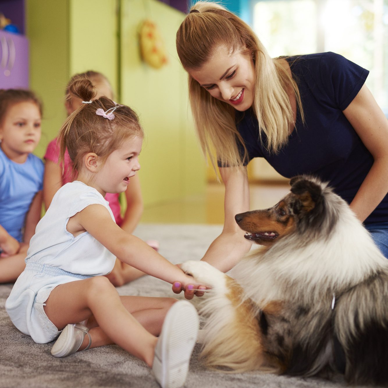 Ein Mädchen gibt einem Therapiehund, die Pfote. Eine Therapeutin unterstützt dabei.